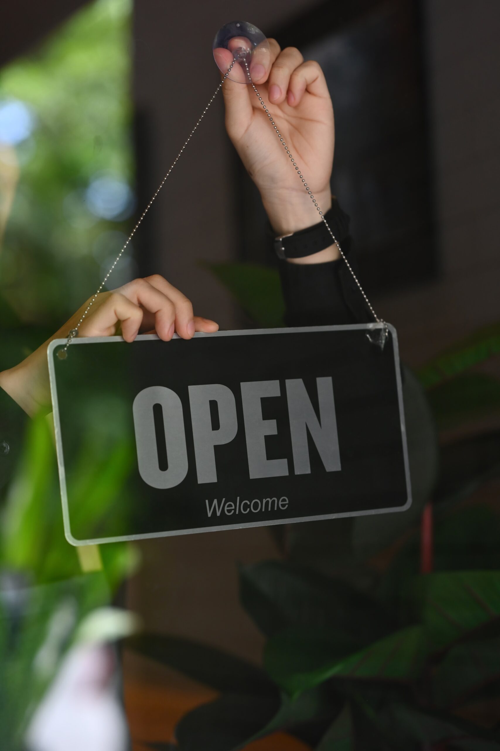 Person holding an 'Open' sign with a 'Welcome' message in a business setting.