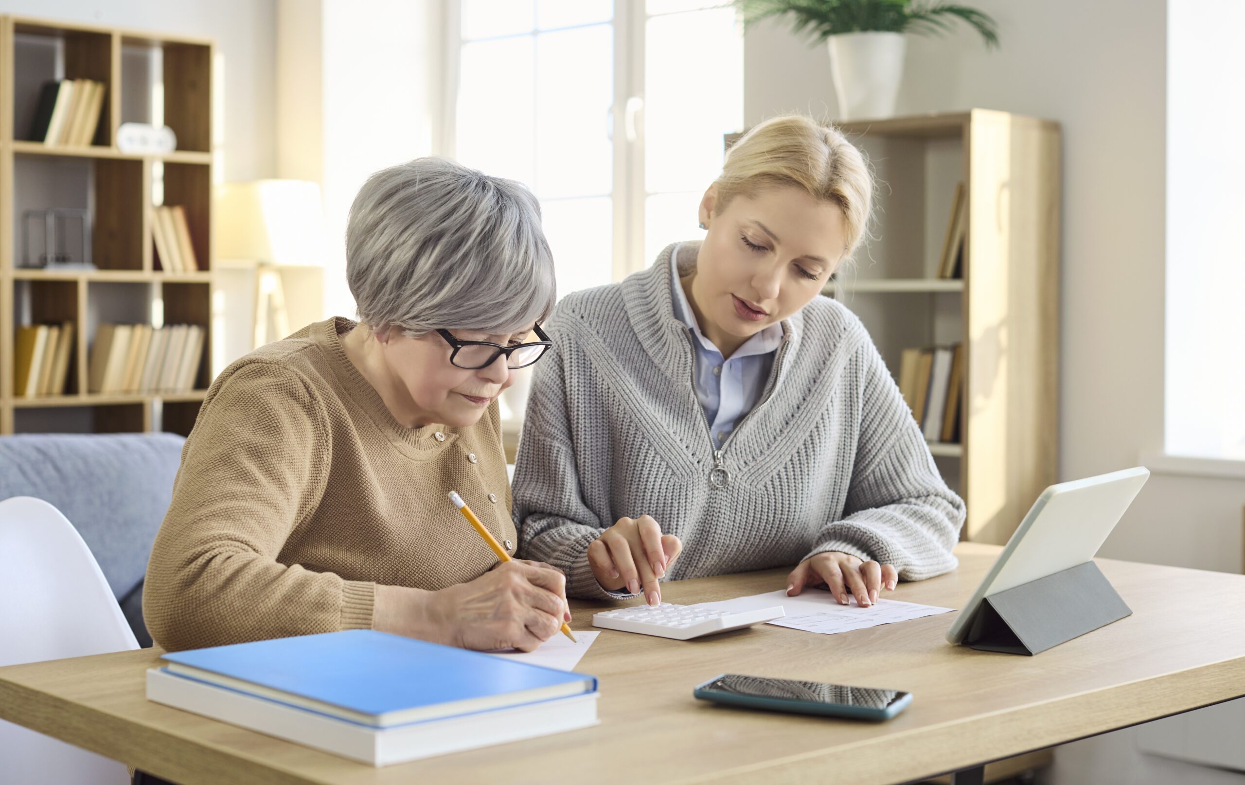 Two women working together on tax preparation at a desk with a tablet and books.